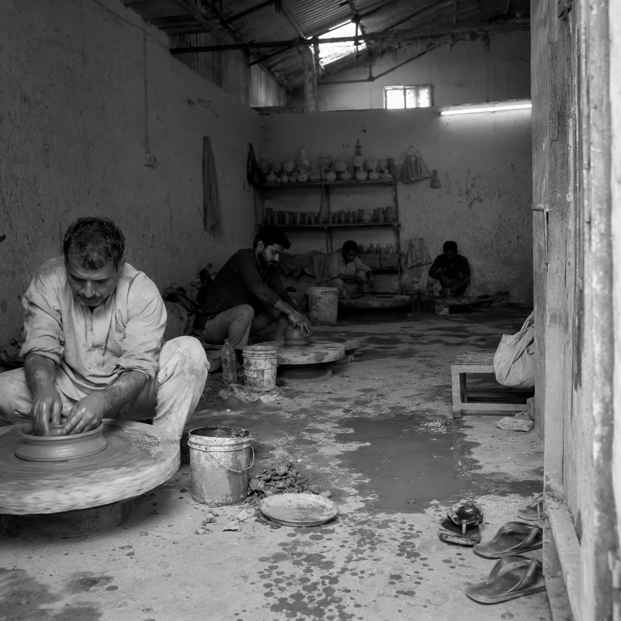 Black and white photograph of a pottery workshop with people working on ceramic mugs